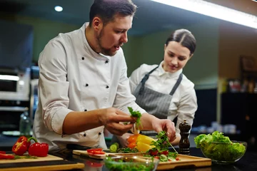 Foto op Plexiglas Koken Chef overlegt zijn stagiair tijdens het koken van salade