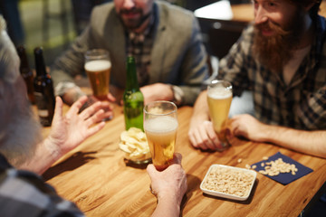 Beer in glasses and group of talking men gathered in pub