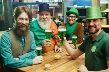 Group of friendly men in traditional costumes toasting with glasses of beer in pub