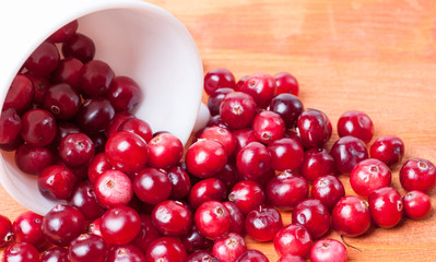 White cup from spilling out of it cranberries on a wooden background