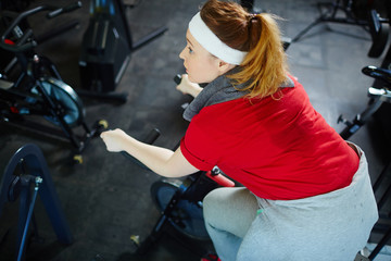 Fototapeta na wymiar Above view portrait of obese sweaty woman determined to lose weight by working out on bicycle machine in gym