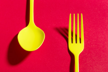 Set of yellow cutlery casting a shadow on red background