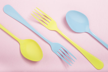 Spoons and forks yellow and blue on pink background