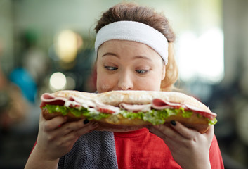 Closeup portrait of young obese woman holding big fattening sandwich in front of her face