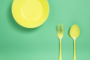 Set of a yellow plate, spoon and fork on green background