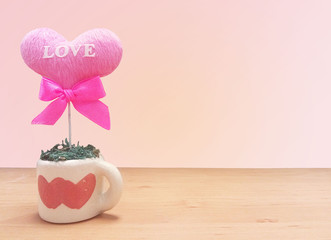 heart-shape flower with the word "LOVE" and  pink bow in a flowerpot on the desk in orange-pink background