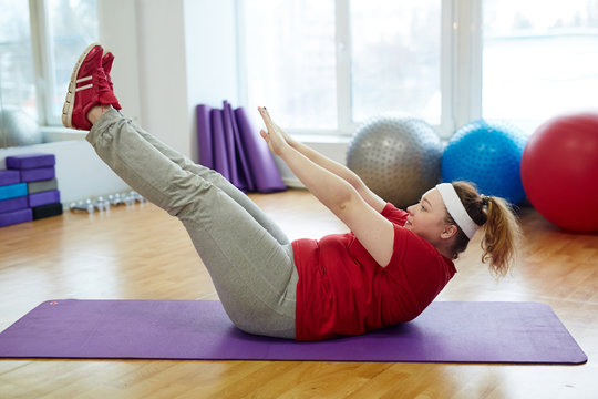 Side View Portrait Of Determined Obese Woman Working Out In Fitness Studio: Performing Toe Tap Straight Leg Sit Ups On Yoga Mat