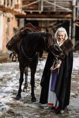 Portrait of a young blond woman in a black cloak with a horse.