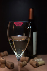 bicchiere di vino bianco con impronta rossetto rosso. sullo sfondo offuscata bottiglia di vino e sughero dispersi.