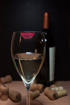 Foto Stock bicchiere di vino bianco con impronta rossetto rosso. sullo  sfondo offuscata bottiglia di vino e sughero dispersi. | Adobe Stock