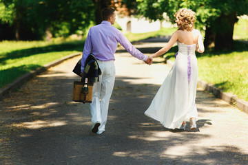 Bride and groom hold their hands tender walking with basket for picnic