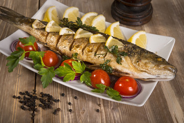 healthy food: two fried sea bass fish served with tomatoes and vegetables on big wooden board over table