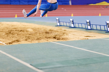 Sportswoman jumping into sandpit on triple jump competition in track and field championship