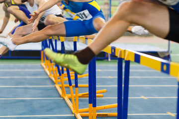 sportsmen running hurdles sprint race in indoor track and field competition