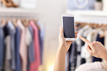 Female hand holding smartphone in clothes shop