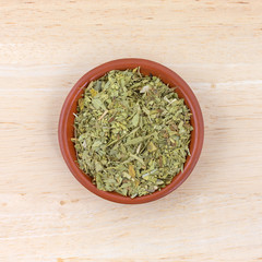 Top view of a small bowl filled with cut and sifted senna leaf on a wood table.