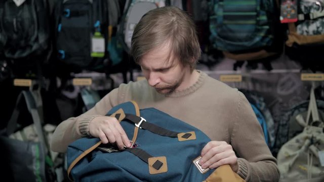 Young man purchasing stylish backpack in extreme tourism shop