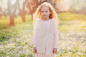 spring portrait of beautiful child girl with curly long hair walking outdoor in blooming garden