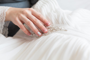 Bride's hands with simple manicure touching wedding dress