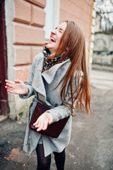 Young model girl in a gray coat with leather handbag on shoulders play with her hairs and posed...