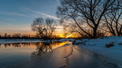 Scenic evening winter landscape. beautiful glow Dramatic sunset over the river to the coast suburb...