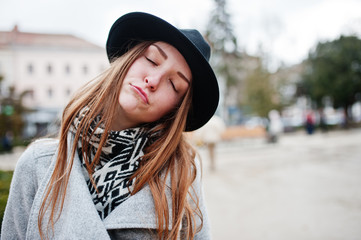 Close up portrait of funny young model girl in a gray coat and black hat with closed eyes and dreaming at street of city.