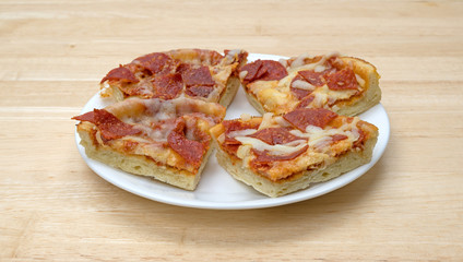 Personal size pepperoni pizza slices on a white plate atop a wood table.