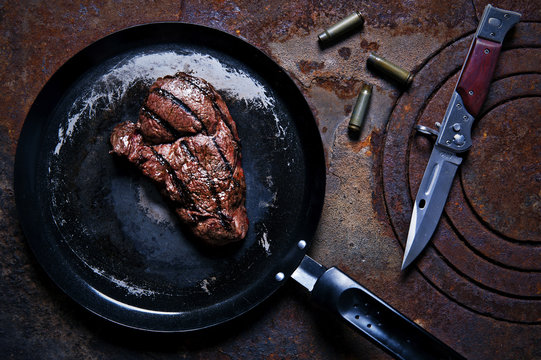 Beef steak in a frying pan standing on the rusty burner