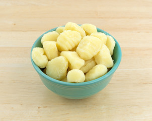 Plain potato gnocchi in a green bowl atop a wood table.