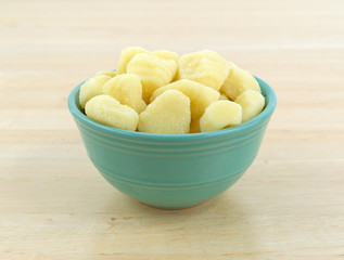 Plain potato gnocchi in a green bowl atop a wood table.