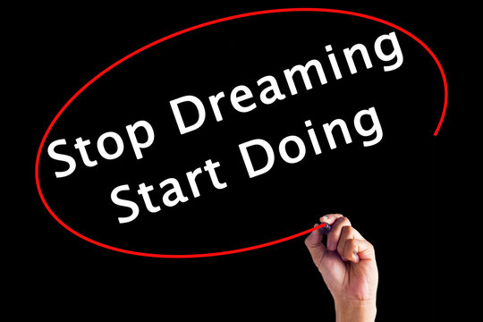 Hand Writing Stop Dreaming Start Doing with a marker over transparent board.