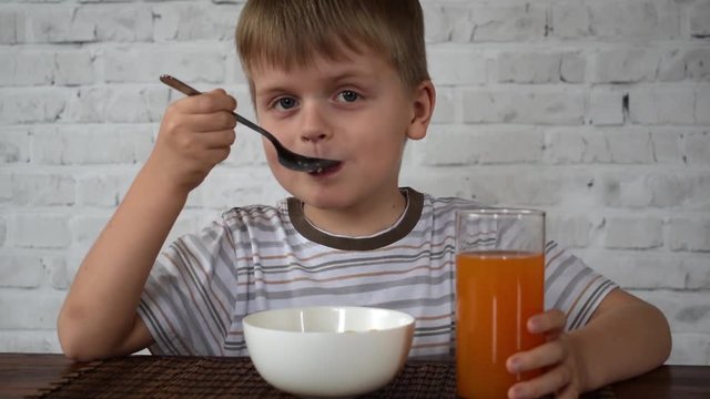 Boy with corn flakes and juice eating from wooden table