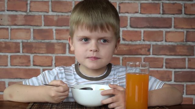 Cute little boy eating corn flakes on breakfast and drinking juice