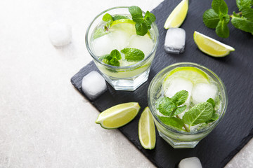 Cold refreshing summer lemonade mojito in a glass on a slate board and stone background.