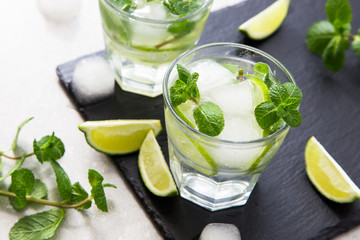 Cold refreshing summer lemonade mojito in a glass on a slate board and stone background.