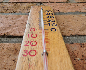 Wooden temperature meter hanging on red brick wall
