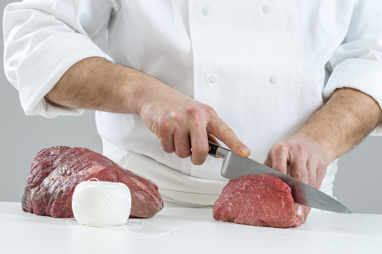 Closeup of the hands of a butcher cutting slices of raw meat off a large loin