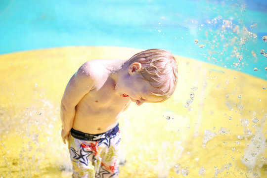 Happy Child Playing At Water Splash Park On Summer Day