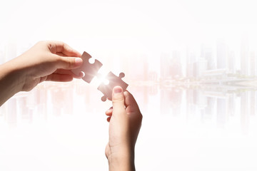 Hands holding jigsaws with the blurred cityscape background concept for business success.