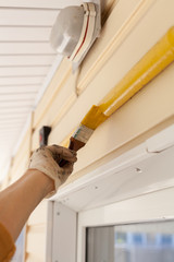 Worker with gloves colors the metal gas pipe of yellow paint with a brush with a wooden handle.