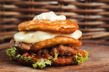 Delicious hamburger potato pancakes with meat, lettuce, cheese, tomatoes on wooden board.