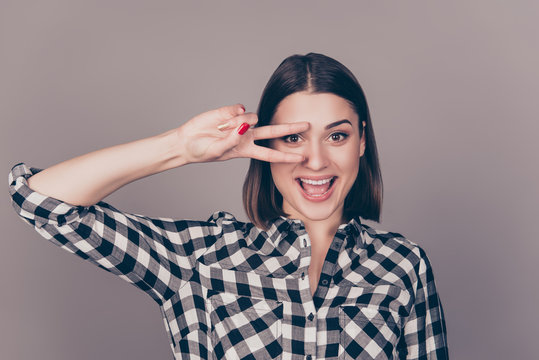 Young happy smiling woman in checkered shirt making victory, positive, peace sign on her eye