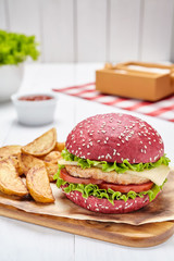 Red burger with beef, cheese, onions, tomatoes, lettuce served with potato fries on a wooden board.