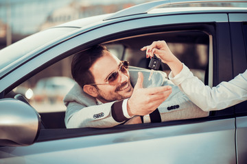 Young man receiving car key from saleswoman