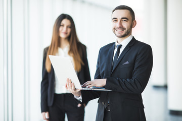 Young and confident businessman with laptop standing in front of business woman