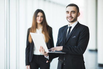 Young and confident businessman with laptop standing in front of business woman