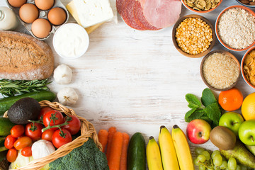 Variety of fruits and vegetables, cereals, ham, cheese, eggs, bread on the white wooden table, top view, copy space, selecitve focus
