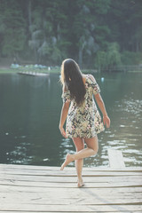 Back view of lady walking on wooden pier near the pond. Vertical outdoors shot.