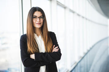 Businesswoman crossed hands portrait in office with panormic windows.
