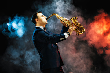 Elegant handsome man playing saxophone in studio against of blue and red smoke